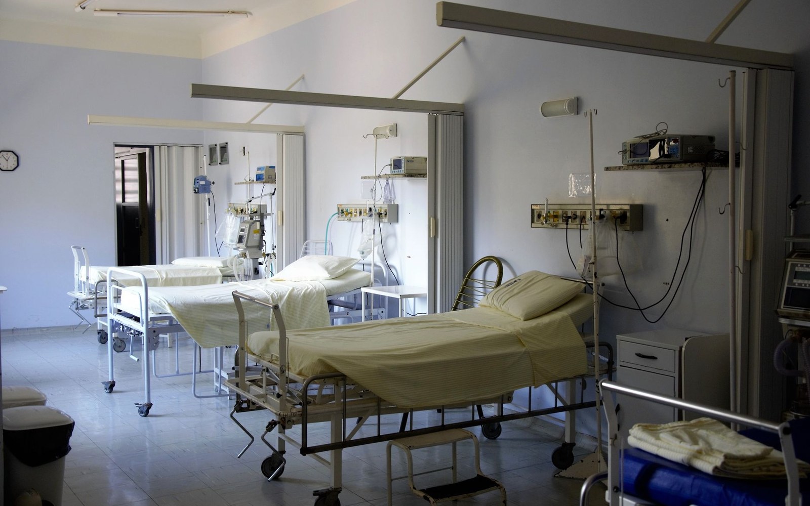 Empty hospital ward with several curtain-partitioned beds and medical monitors along the walls