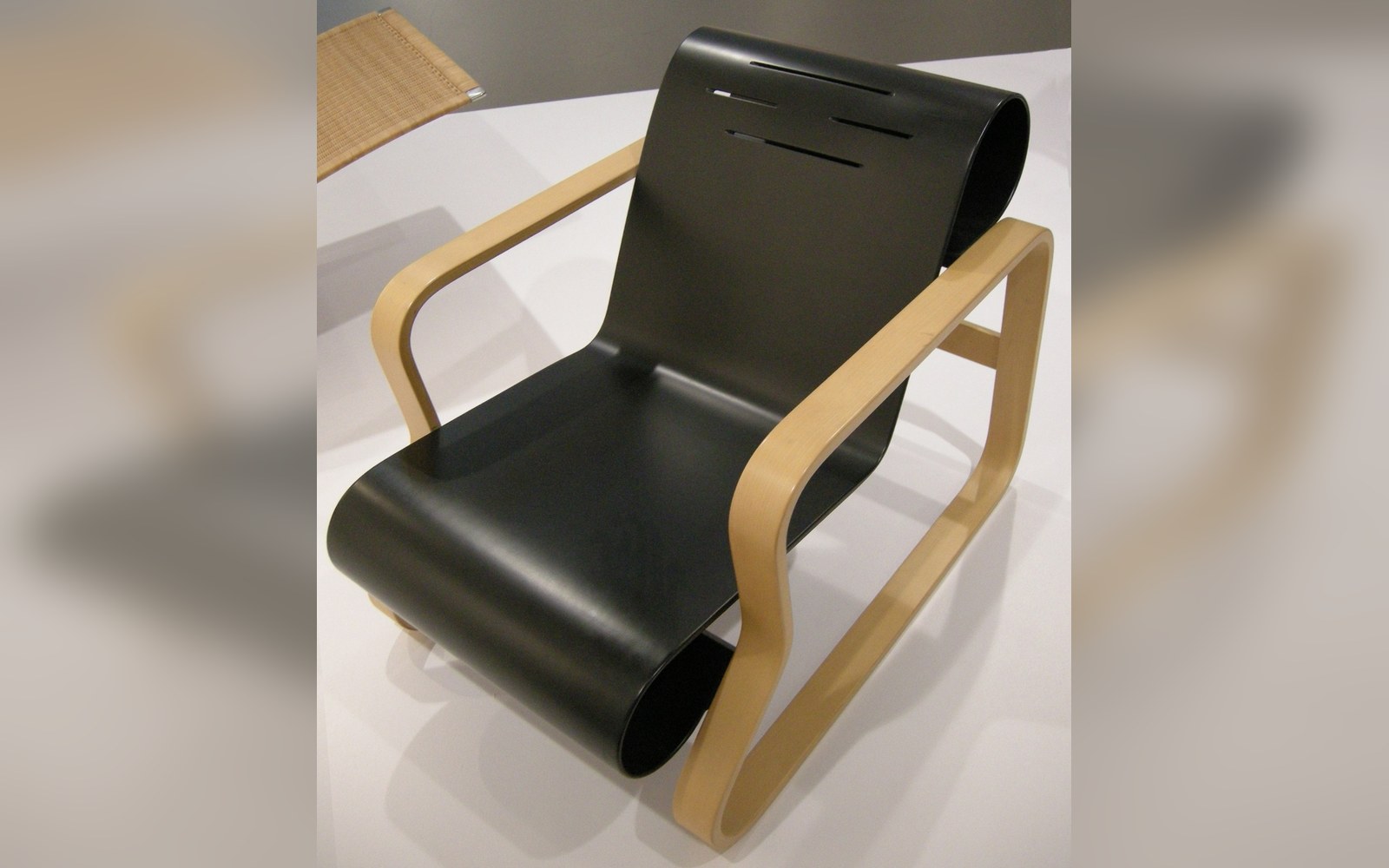 Bent plywood armchair with a curved black seat and light wood frame