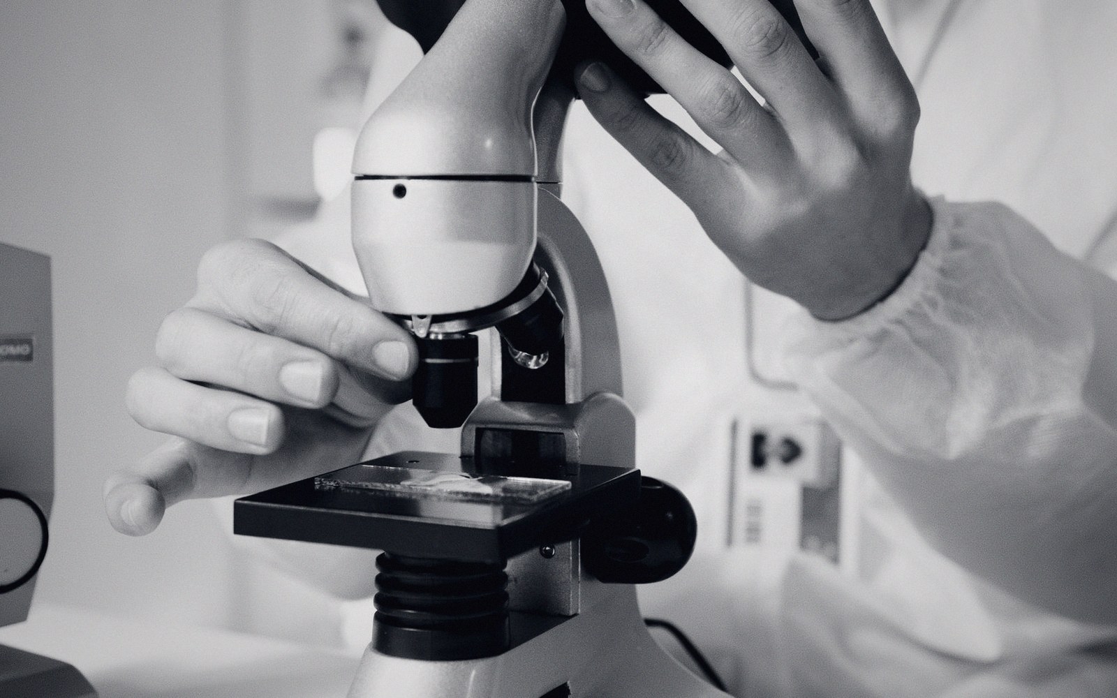 Close-up of hands adjusting a microscope with a slide in a lab