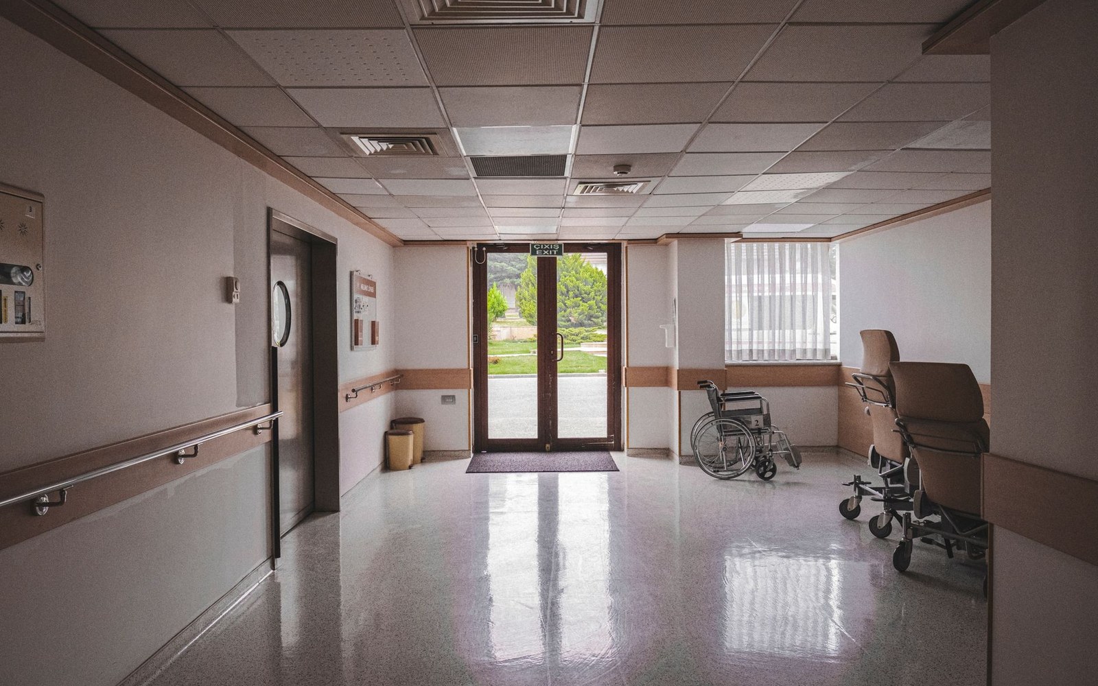 Empty hospital corridor with a wheelchair and gurney near glass exit doors