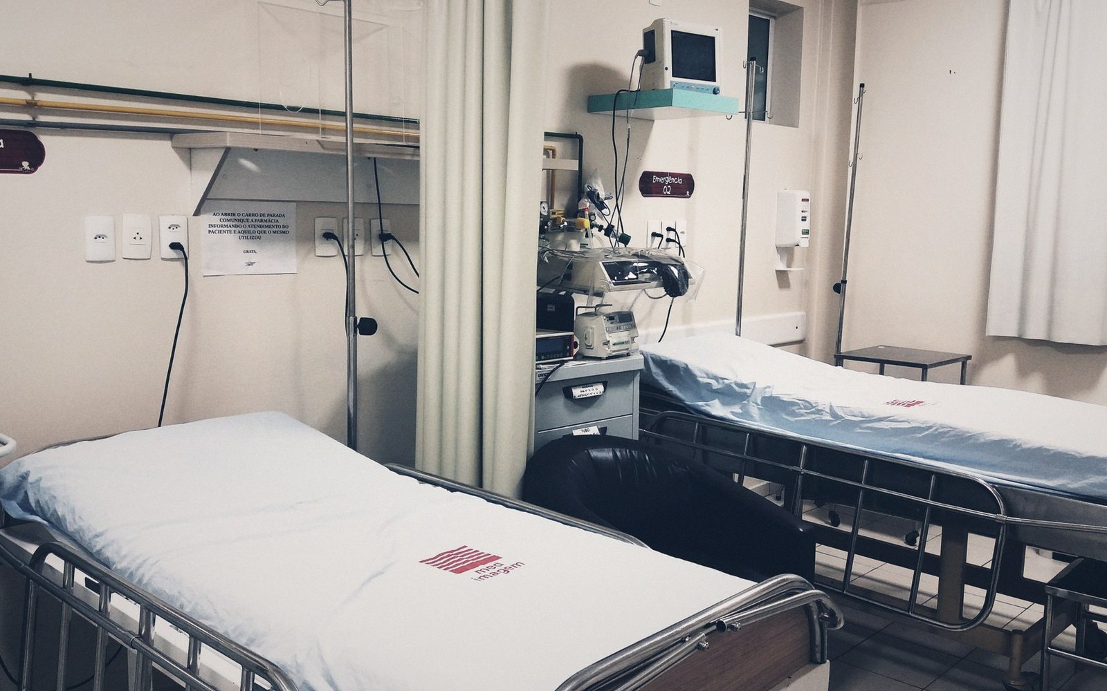 Two hospital beds separated by a curtain, with monitoring equipment on a wheeled stand
