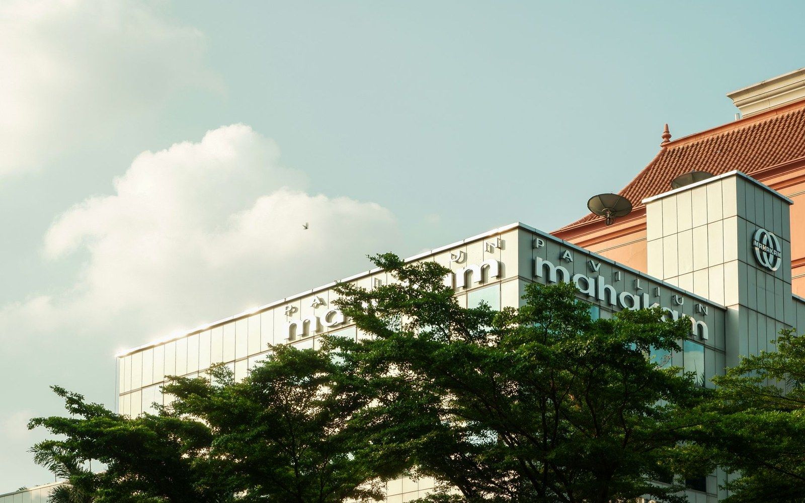 Pavilion Mahakam building facade with tiled roof rising above green treetops